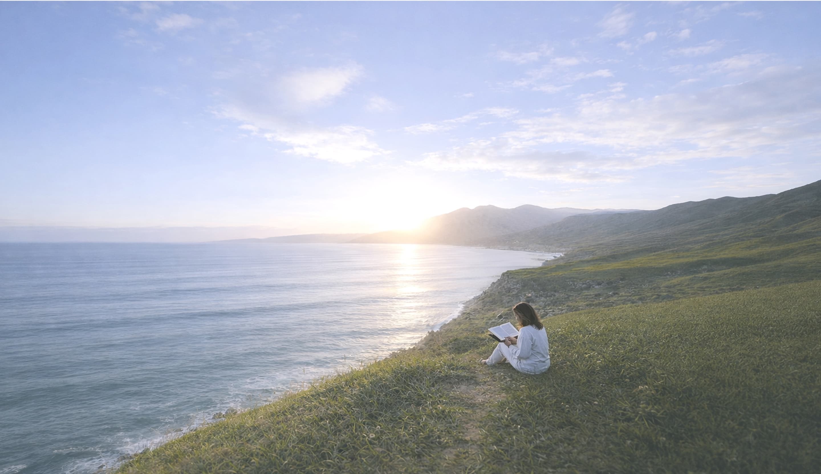 Woman reading on a hillside by the sea